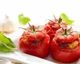Trois tomates farcies au four, garnies d'une farce savoureuse, servies avec des feuilles de basilic frais.