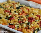 Un vassoio di verdure al forno, con patate, zucchine e pomodorini, condite con pangrattato dorato.