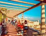 Blick vom Miradouro Lissabon über die Stadt und das Meer. Menschen genießen die Aussicht unter einer hölzernen Pergola.