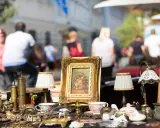 Antikviteter och kuriosa på ett bord, kanske på en loppmarknad i Stockholm. En blomstermålning i guldram, små lampor och porslin.