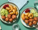 Två tallrikar med köttbullar, småpotatis, gurka och lingonsylt. En perfekt snabb middag för två.