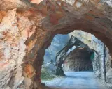 Un túnel natural en la ruta del silencio Teruel, con paredes de roca rojiza y un camino que se adentra en la montaña.