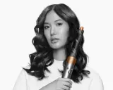 Frauenhaar wird mit einem Airwrap-Lockenstab zu perfekten Wellen geformt.