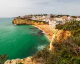 Blick auf die sonnenverwöhnte **Carvoeiro Altstadt** mit ihren weißen Häusern, die sich an die Klippen schmiegen. Der goldene Sandstrand lädt zum Verweilen ein, während das smaragdgrüne Meer sanft an die Küste brandet.