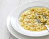 Tortellini in brodo, uno dei cibi tipici dell'Emilia Romagna, serviti in una ciotola bianca con un cucchiaio.
