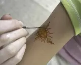Rysowanie słońca z uśmiechem jako tatuaż z henny na ramieniu.