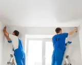 Dwóch fachowców na drabinach montuje biały sufit napinany, tworząc gładką powierzchnię.