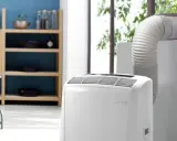 Climatiseur Rowenta portable, avec son tuyau d'évacuation dirigé vers une fenêtre. Un meuble de cuisine est visible à gauche.
