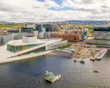 Il porto di Oslo con l'Opera House e moderni edifici. Barche navigano nell'acqua scura.