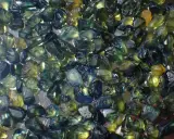 Un mucchio di zaffiri grezzi australiani, con sfumature verdi, blu e gialle. Il loro valore è legato alla rarità e alla bellezza di queste gemme naturali.