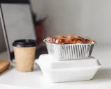 Gotowe jedzenie na wyjazd: zapiekanka w folii aluminiowej i kawa w kubku. Idealne na szybki lunch przy laptopie.