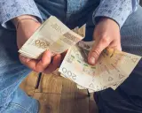 Ręce trzymające stos banknotów 200 zł. To może być wynagrodzenie za urlop, które pozwoli na zasłużony odpoczynek.