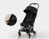 Elegancki czarny wózek Cybex Coya z miedzianymi detalami. Widoczna lupa pokazuje łatwe zapinanie pasów.