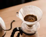 Frisch aufgebrühter Kaffee blubbert im Papierfilter. Ein Wasserkocher steht bereit, um das Ritual des Kaffeefilter selber machen zu beginnen.