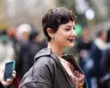 Frau mit einem lässigen Pixie-Cut, dunklem Lippenstift und Lederjacke lächelt in die Kamera.