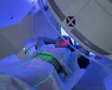 Pacjentka leży pod aparatem do radioterapii, na jej ciele widoczne są zielone i czerwone linie naprowadzające.