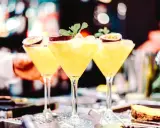 Trzy kieliszki z orzeźwiającą mango margarita, ozdobione połówkami marakui i listkami mięty, gotowe do podania.
