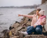 Mama z córką siedzą na kamieniach nad jeziorem. Mama wskazuje coś palcem, a dziewczynka się śmieje. To świetne gąski atrakcje dla dzieci.