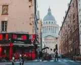 Urokliwa uliczka w paryskiej dzielnicy łacińskiej z czerwonym bistro i majestatycznym Panteonem w tle.