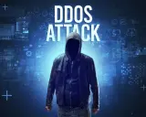 Anonimowa postać w kapturze na tle cyfrowych danych. Wielki napis "DDOS ATTACK" wyjaśnia, ddos co to.