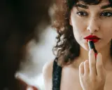 Donna con capelli ricci applica un trucco con rossetto rosso vibrante, creando un look audace e seducente.