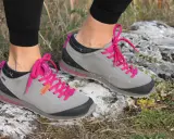 Szare buty trekkingowe Aku Bellamont z jaskrawymi, różowymi sznurówkami na kamienistym, trawiastym podłożu.