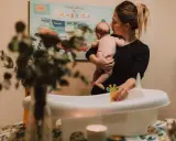 Mamma håller sitt barn redo för bad. Frågan "hur ofta bada bebis" dyker upp när man förbereder badkaret med leksaker.