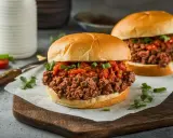 Zwei saftige Sloppy Joes auf einem Holzbrett, garniert mit Frühlingszwiebeln und Tomaten.