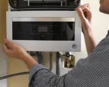Ręce technika montują panel sterowania kotła gazowego. Pamiętaj, co ile lat wymiana pieca gazowego zapewni bezpieczeństwo i efektywność.