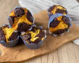 Schokoladen-Vanille-Zupfkuchen-Muffins in blauen Papierförmchen auf einem Holzbrett.