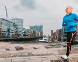 Frau mit kurzen Haaren läuft im Hafen. Sie trägt Sportkleidung und Schuhe. Mit Laufen abnehmen ist ihr Ziel.
