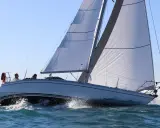 Un voilier Jeanneau Symphony navigue sur une mer agitée, ses voiles blanches gonflées par le vent. Un avis positif pour ce bateau.
