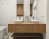 Nowoczesna łazienka z dwoma umywalkami na drewnianej szafce. Minimalistyczny design, białe ceramika i ciepłe drewno tworzą harmonijną przestrzeń.