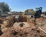 Excavadora amarilla trabajando para cavar zanjas en un día soleado. Un hombre supervisa la obra.