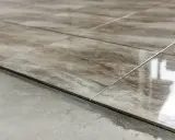Detalle de las partes de un piso: baldosas de cerámica con veteado marrón y gris, recién colocadas sobre una base de cemento.