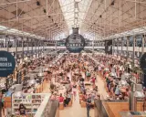 Belebter Time Out Market in Lissabon. Menschen sitzen an langen Tischen, essen und unterhalten sich. Überall gibt es Essensstände.