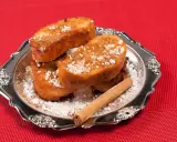Torrijas de Semana Santa espolvoreadas con azúcar glas y canela, servidas en un plato plateado con una rama de canela.