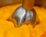 Metalowa końcówka blendera zanurzona w gęstym, pomarańczowym puree z dyni.