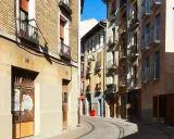 Calle adoquinada con edificios coloridos y balcones. Un cartel de "haya real estate" podría estar en uno de estos locales.