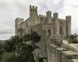 Die Obidos Burg thront majestätisch auf einem Felsen. Fahnen mit dem Namen "Obidos" wehen im Wind.