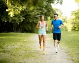 Ein lachendes Paar joggt glücklich durch einen sonnigen Park. Sie genießen die frische Luft und die Bewegung – das ist, was Joggen bringt.