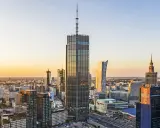 Warszawski krajobraz zdominowany przez wieżowce, w tym najwyższy hotel w Warszawie, lśni w złotym świetle zachodzącego słońca.