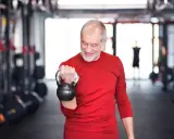Ein älterer Mann mit Bart trainiert im Fitnessstudio mit einer Kettlebell. Ein Beispiel für Krafttraining ab 60 Jahren Trainingsplan.
