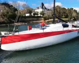 Le voilier Pogo RC, blanc et rouge, est amarré à un ponton. Une personne en blouson rouge est à bord.