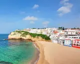 Traumhafte Küstenlandschaft in Portugal, Carvoeiro: Weiße Häuser schmiegen sich an grüne Klippen, daneben ein goldener Sandstrand und türkisfarbenes Meer.