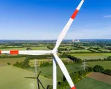 Windkraft Energie: Ein riesiger Windpark dominiert die Landschaft, umgeben von grünen Feldern und Bäumen. Im Hintergrund sind Kühltürme zu sehen.