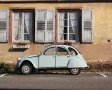 Jasnoniebieski, zabytkowy Citroen 2CV, jeden z tych klasycznych, francuskich modele stare, stoi przed kamiennym domem z drewnianymi okiennicami.