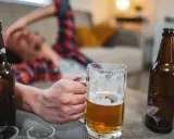 Mężczyzna leży na kanapie, trzymając kufel piwa. Wokół leżą puste butelki. Czy to oznacza, co przyspiesza spalanie alkoholu?