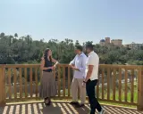 Tres personas conversan en la terraza de la cafetería mirador Elche, con un frondoso palmeral y el casco antiguo de la ciudad al fondo.