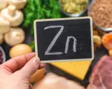 Tabliczka z napisem "Zn" na tle produktów bogatych w cynk: mięso, ryby, fasola, grzyby, jajka, ser, nasiona.
